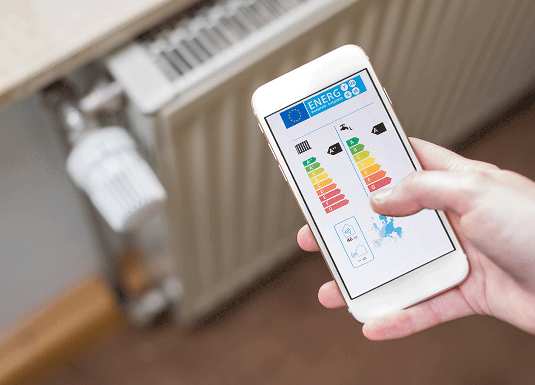 Hand hält Smartphone mit Energielabel vor Heizkörper